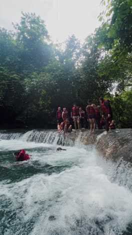 People-wearing-life-jackets-jumps-off-and-swimming-into-the-mountain-river