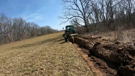 Niedrige-Winkelansicht-Eines-John-Deere-Traktors-Mit-Einem-Angebauten-Lader-Schleppt-Einen-Pflug,-Um-Den-Boden-Umzugraben,-Als-Ersten-Schritt-Bei-Der-Vorbereitung-Des-Feldes-Für-Die-Frühjahrsbepflanzung