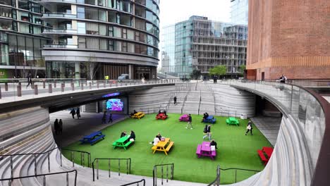 People-At-Public-Seating-Area-With-Colorful-Picnic-Tables-At-Battersea-Power-Station-In-London,-UK