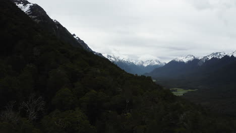 Aerial-View-Of-Forested-Mountainside-And-Snow-Capped-Mountains-In-Horizon,-Eglinton-Valley-In-Fiordland,-New-Zealand