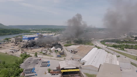 Wide-aerial-pan-across-a-busy-highway-with-a-large-industrial-fire-being-worked-on-by-emergency-services