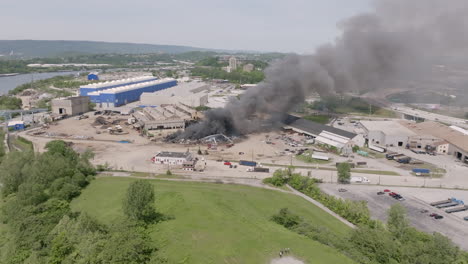 Wide-aerial-footage-flying-towards-a-large-industrial-fire-in-Chattanooga,-TN-with-bikers-pulling-up-on-a-hill-to-watch