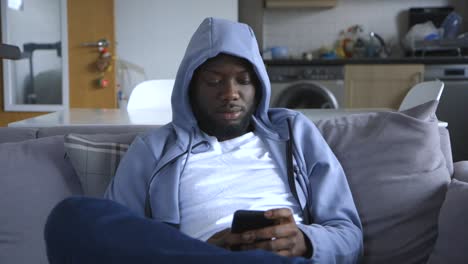 Black-Male-Sitting-On-Couch-And-Texting-In-Lounge-Room
