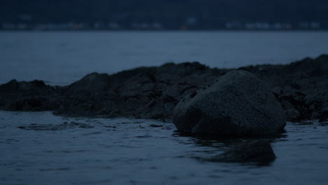 Rocks-surrounded-by-water-with-blurred-car-passing-on-land-behind