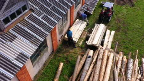 Workers-stack-freshly-cut-planks-at-sawmill-on-side-of-building,-aerial-bird's-eye-view