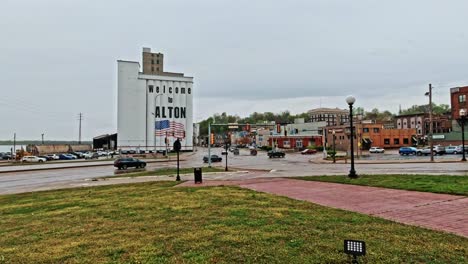 Ardent-Mill-In-Alton-Mit-„Willkommen-In-Alton“-Fassade-Und-Wandgemälde-Mit-Amerikanischer-Flagge,-Verkehr-Fließt-An-Kreuzung,-Illinois,-USA