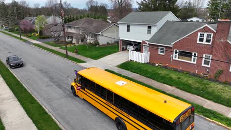 Yellow-school-bus-stopping-on-road-of-American-neighborhood