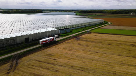 Semi-truck-arriving-to-massive-industrial-tomato-greenhouses,-aerial-drone-view