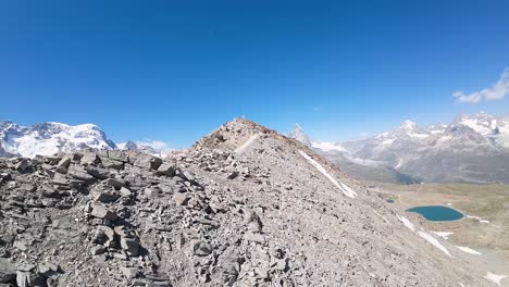 Flight-over-a-hiking-trail-at-Alps-mountains-in-Gornergrat,-Zermatt,-in-Switzerland-with-the-reveal-view-of-a-beautiful-glacier