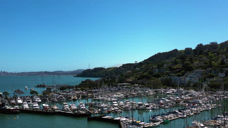 Aerial-view-over-boats-at-Sausalito-marina,-revealing-the-Golden-Gate-bridge,-in-sunny-California,-USA