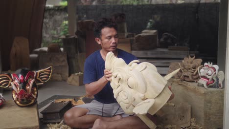 Wood-Carver-Blowing-The-Dust-Off-On-Barong-Bangkal-Mask,-Mythical-Animal-That-Has-Strength