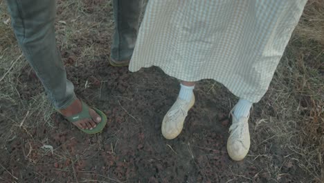 Two-people-standing-on-a-dirt-path,-focus-on-their-contrasting-footwear