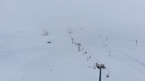 Aerial-view-of-snow-covered-ski-slopes-with-very-few-people-skiing-foggy-winter-day