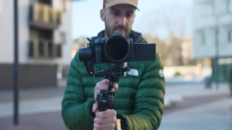 Vlogger-with-cap-and-green-jacket-testing-innovative-modern-FeiyuTech-Scorp-2-stabilizer-gimbal-with-Canon-professional-camera-mounted