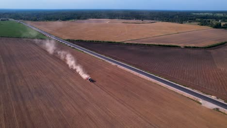 Tractor-ploughs-across-dirt-field-with-trail-of-dust-rising-into-air,-aerial