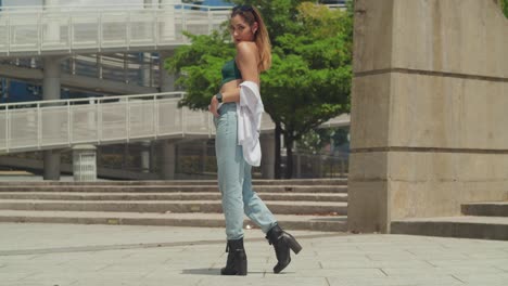 Immersed-in-discovery,-a-young-girl-in-jeans-and-boots-explores-a-Caribbean-city,-with-tall-buildings-casting-shadows-in-the-background