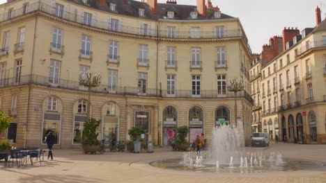Sunny-day-at-Place-Graslin-in-Nantes,-France,-with-people-walking-near-a-fountain,-classic-European-architecture-in-the-background