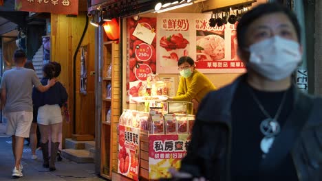 People-wander-through-a-bustling-narrow-lane-flanked-by-food-stalls,-souvenir-boutiques,-and-quaint-gift-shops-in-Jiufen-Old-Street,-a-charming-mountain-village-town-in-Taiwan