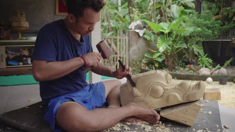 Barong-Woodcarver-Making-Barong-Bangkung,-Old-Pig-Figure-On-Wood-With-A-Chisel-Struck-By-A-Mallet