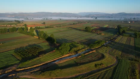 Aerial-View-of-Green-Agricultural-Parcels-Around-European-Farm-at-Sunrise-in-Spring,-Morning-Flight