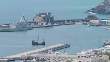 Die-Antike-Trifft-Auf-Die-Gegenwart:-Das-Alte-Karavellenschiff-Santa-Maria-Läuft-An-Einem-Blauen-Sommertag-In-Den-Hafen-Von-Funchal-Auf-Der-Insel-Madeira-Ein,-Im-Hintergrund-Ein-Teil-Der-Stadt-Und-Ein-Militärboot