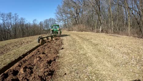 Following-a-John-Deere-tractor-towing-a-plow-through-a-dormant-field-in-early-spring-in-the-Midwest