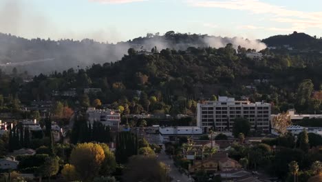 Fire-in-Encino-Hills-neighborhood-of-high-end-homes,-aerial-rising-of-smoke-filled-sky
