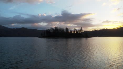 Langsame-Luftaufnahme-Mit-Dolly-über-Dem-Wasser-In-Richtung-Einer-Insel-Auf-Dem-Whiskeytown-Lake-Mit-Dem-Sonnenaufgang-Im-Hintergrund