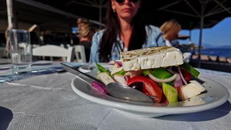 Woman-cant-wait-to-eat-Greek-salad-with-sea-view-behind,-motion-forward-view