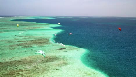 Kite-surfers-gliding-over-the-clear-turquoise-waters-by-the-barrier-reef-of-los-roques,-aerial-view