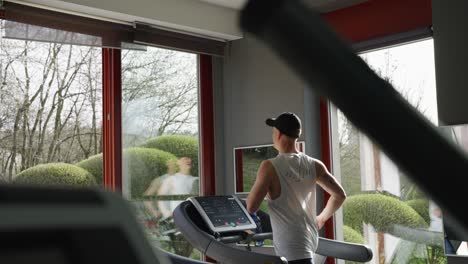 Static-shot-of-person-run-on-treadmill-at-indoor-gym-with-large-windows,-Prague