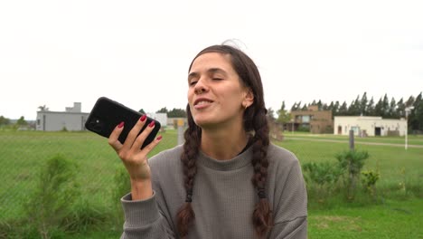 Young-woman-with-braids-and-nose-piercing-talks-on-speaker-phone-outdoors