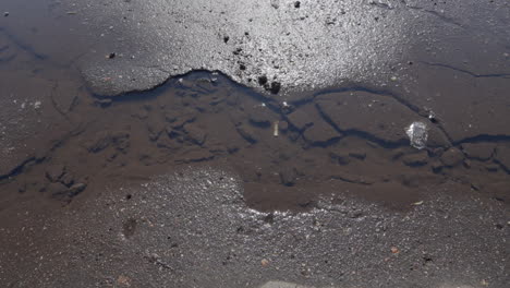 Selbst-Geschaffener-Wasserstrom-Auf-Sandigem-Und-Schlammigem-Braunem-Asphalt,-Der-Die-Gefahren-Einer-Schlecht-Gewarteten-öffentlichen-Straße-Verdeutlicht