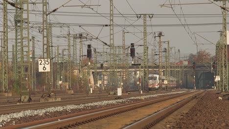 Vías-De-Ferrocarril-Que-Se-Extienden-Hacia-Un-Horizonte-De-Hora-Dorada-Con-Trenes-Y-Señales