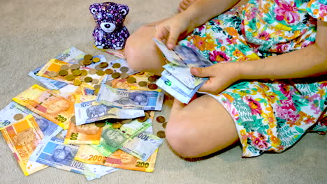 Girl-counts-stack-of-R100-rand-South-African-notes-on-top-of-other-banknotes