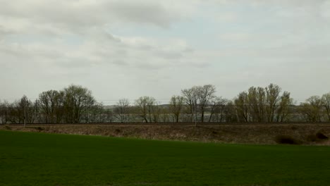 Red-locomotive-pulls-freight-train-across-rural-landscape,-cloudy-sky