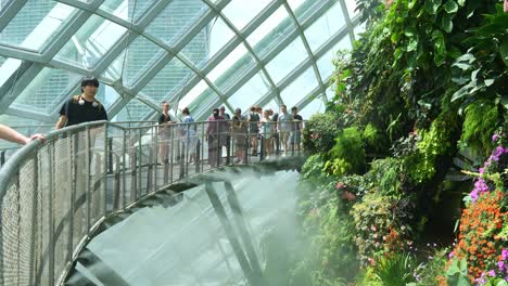 Tourists-stroll-along-the-aerial-walkway-in-Cloud-Forest-greenhouse-conservatory-at-Gardens-by-the-Bay-in-Singapore,-misty-water-spray-used-for-temperature-control,-creating-a-magical-atmosphere