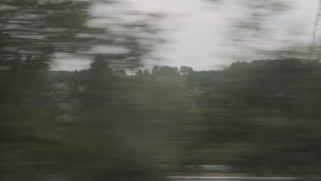 Verschwommene-Landschaft-Aus-Einem-Zugfenster-Mit-Wald-Und-Vorbeifahrenden-Autos,-Bewegungsunschärfe-Effekt