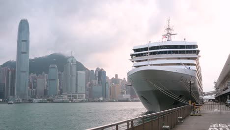 Ein-Großes-Kreuzfahrtschiff-Liegt-Am-Ocean-Terminal-Im-Victoria-Harbour-Vor-Anker,-Im-Hintergrund-Sieht-Man-Die-Skyline-Von-Hongkong