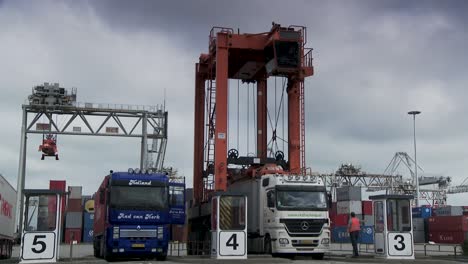 Busy-shipping-port-with-trucks-and-a-large-container-crane-under-cloudy-skies,-transport-logistics-in-action