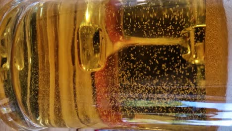 Bubbles-of-beer-rises-in-transparent-glass,-close-up-vertical-view