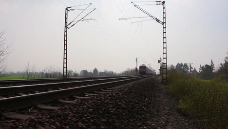 Red-Deutsche-Bahn-train-traveling-on-tracks-through-rural-landscape