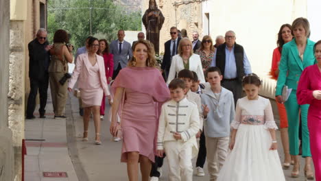 A-family-walks-through-a-quaint-Spanish-village-during-a-child's-First-Communion,-vibrant-and-lively