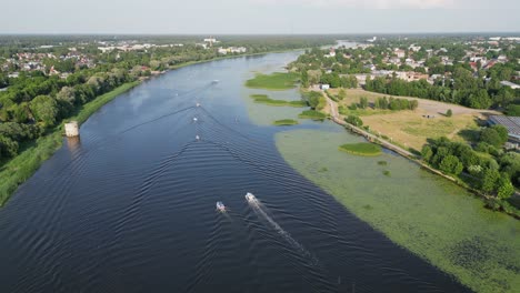 Boats-motor-up-Parnu-River-in-beautiful-green-city-of-Parnu,-Estonia