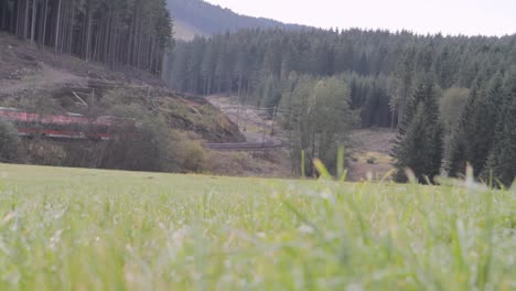 Red-Deutsche-Bahn-train-curving-through-a-lush-green-valley-with-forested-hills,-distant-view