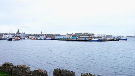 Scenic-view-overlooking-harbour-water-and-moored-boats-towards-Stornoway-town-with-houses,-shops,-and-businesses-in-the-Outer-Hebrides-of-Scotland-UK