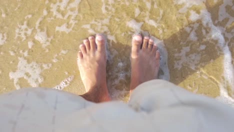 Small-sea-wave-coming-on-the-feet-in-slow-motion,-feet-on-the-sand,-top-down-view