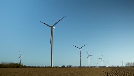 Wind-turbines-gracefully-spin-in-a-clear-blue-sky-above-a-plowed-field-during-the-day,-renewable-energy-concept