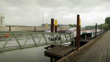 Car-driving-over-green-bridge-near-industrial-zone-by-river,-overcast-day