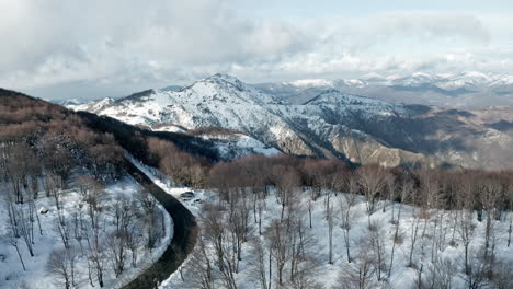 Winter-landscape-aerial-view-of-a-snowy-mountain-road-winding-through-a-forest